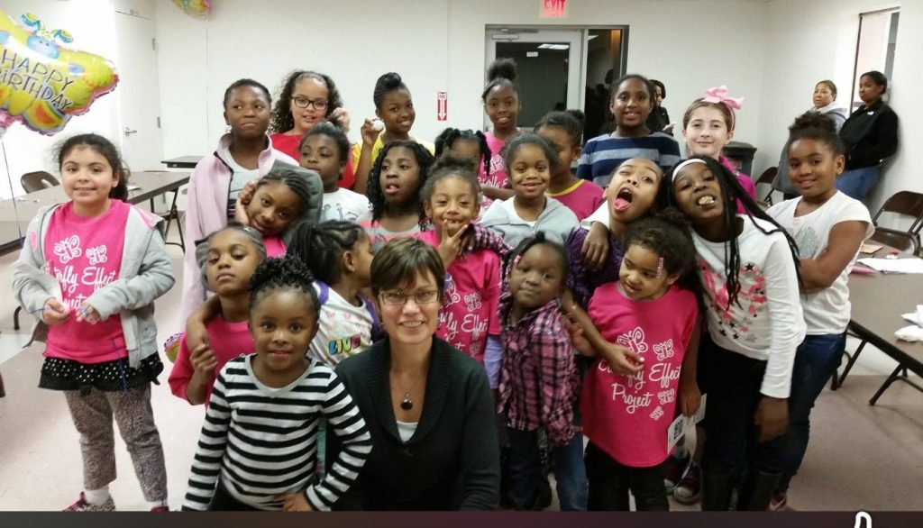 Youth and adults squeeze into a tight group huddle hug indoors.
