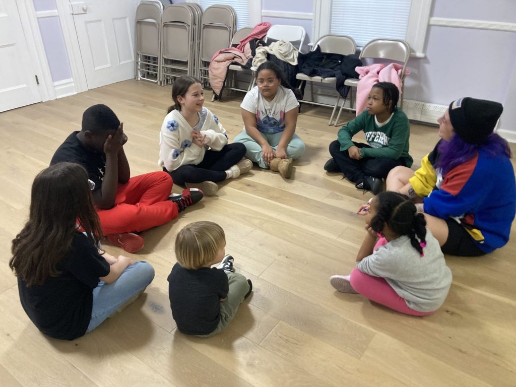 Youth and adults squeeze into a tight group huddle hug indoors.